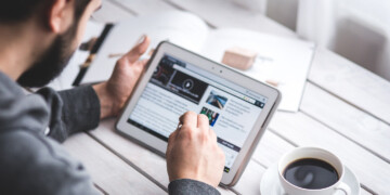 person scrolling on ipad on desk with coffee.