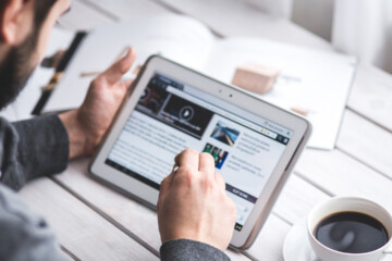 person scrolling on ipad on desk with coffee.