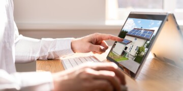 Man in white dress shirt on laptop computer looking at a home with solar panels.