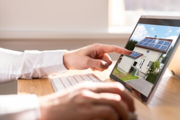 Man in white dress shirt on laptop computer looking at a home with solar panels.