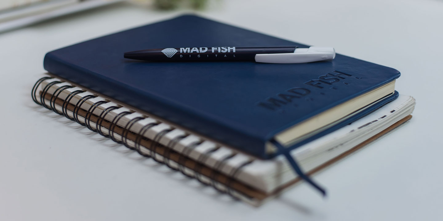 Mad Fish branded pen on top of two notebooks.