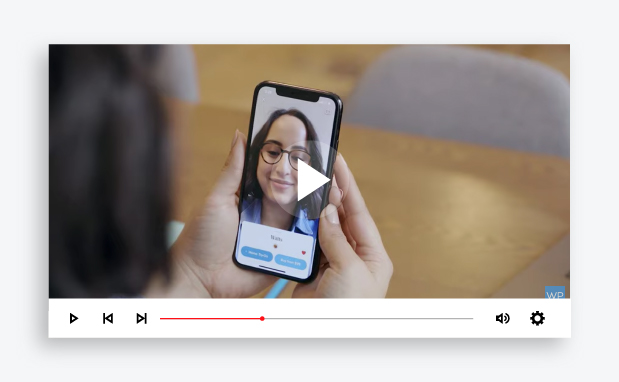 Paused video image of a person using their phone to look at their reflection with new glasses.