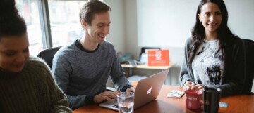 group of people sitting around a table looking at a laptop