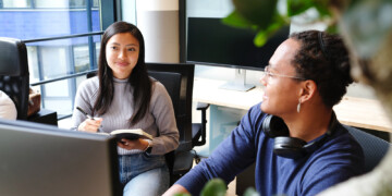 Two people talking, one taking notes, the other showing something on a computer.