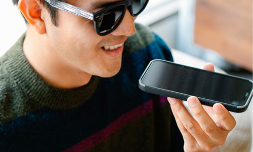 Man wearing sunglasses talking into a phone and smiling.