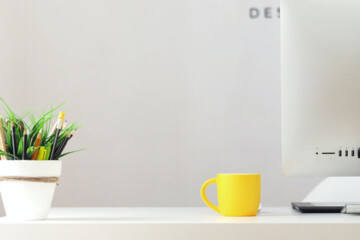 Apple computer on desk with yellow mug and small green plant.