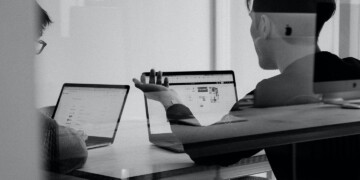 Two people on laptops talking behind a glassdoor.