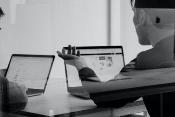 Two people on laptops talking behind a glassdoor.