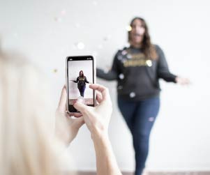 Close up of someone taking a video on a phone of a woman throwing confetti in the air.