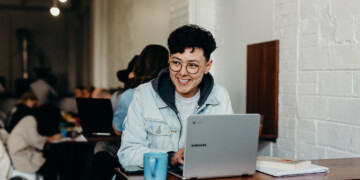 woman working at coffee shop with laptop at a table.