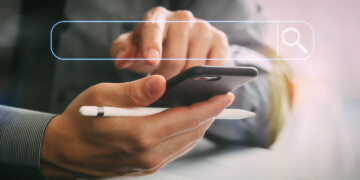 A person poises to touch the screen of a cell phone while holding a white pen.