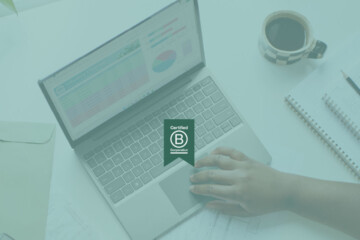 A certified B Corp badge logo overlaid on top of a background image of someone using their laptop.