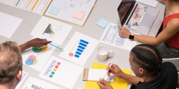 A group of coworkers gathered at a table with sheets of paper laid on on the desk.