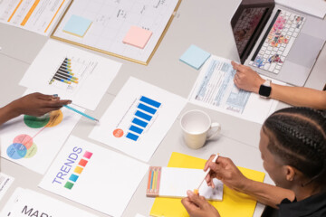 A group of coworkers gathered at a table with sheets of paper laid on on the desk.