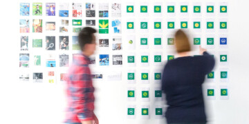 Two people looking at books and brand logos hanging on a white wall.