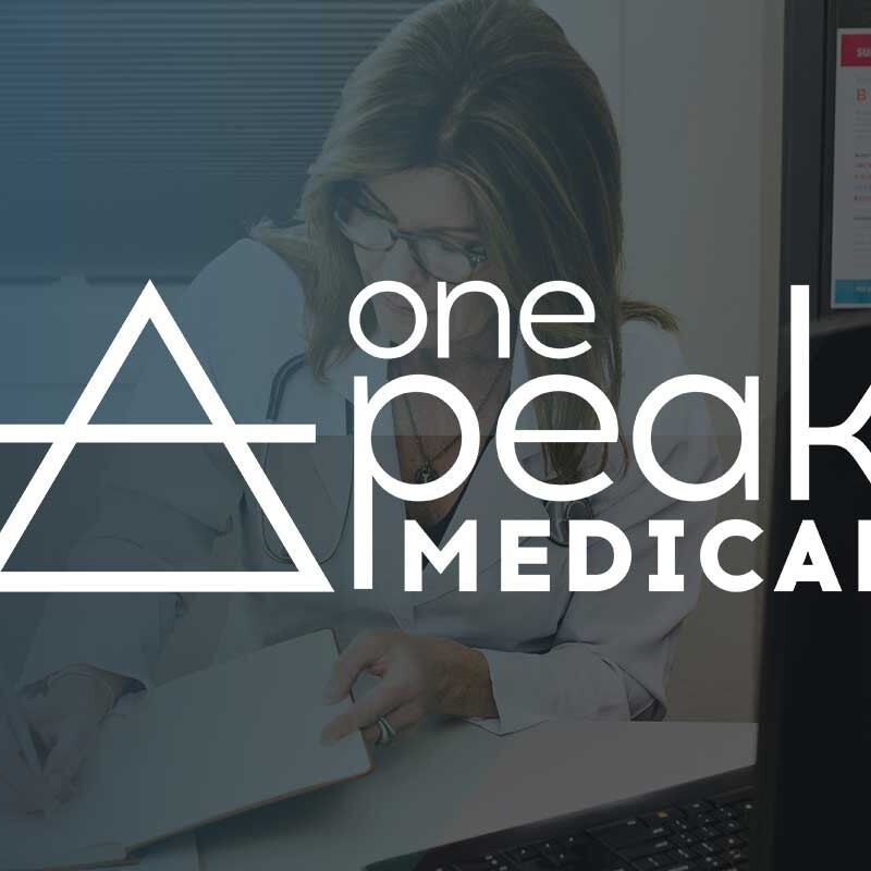 OnePeak Medical founder and owner, Nisha Jackson sits at her desk in front of a computer with their logo overlaid on top.