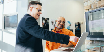 Two men in an office review SEO performance on a laptop.