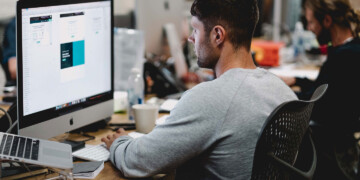 A man designing a website on an iMac at his desk.