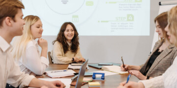 A group of five millennial coworkers sit at a conference table while reviewing a marketing strategy.