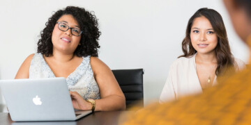 Two millennial women sit at a conference room table.