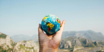 A hand holding a small globe in front of mountain scenery.