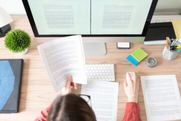 Person sitting at a desk, reading a print out and working on their desktop.