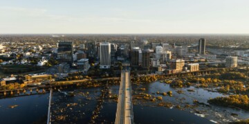 Aerial view of downtown Richmond, Virginia skyline with the James River in the foreground, showing the city's bridges, high-rise buildings, and fall foliage along the riverbanks