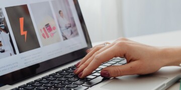 Close-up of a woman's hands typing on a laptop displaying a content or news website.